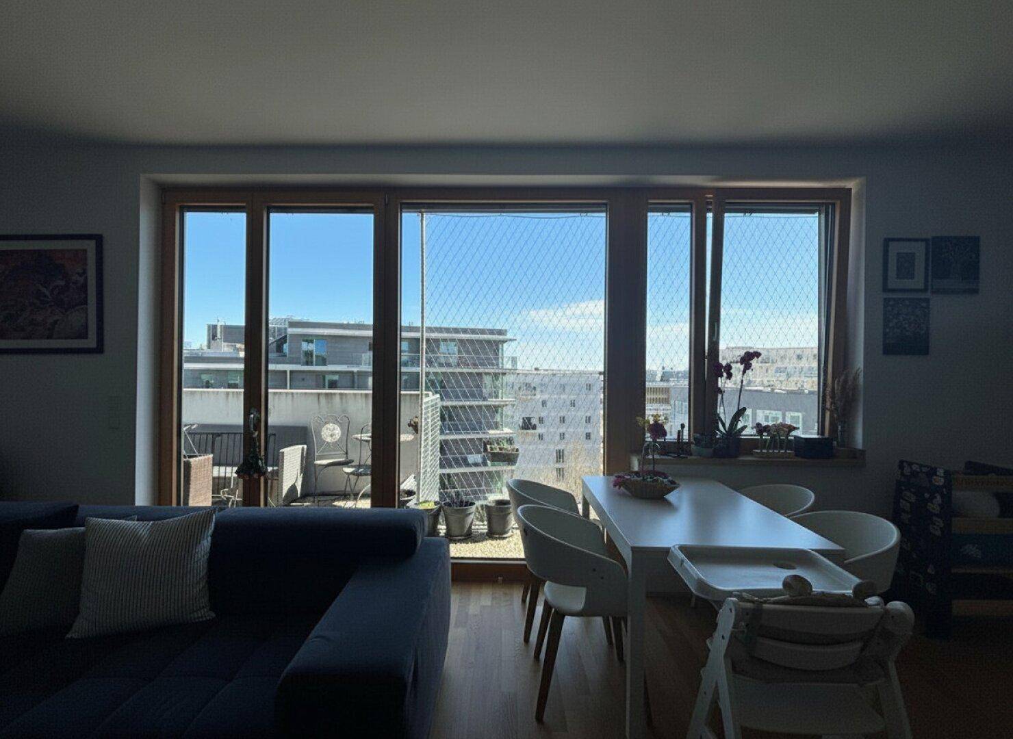 Heller Wohn- und Essbereich mit großen Fenstern und Zugang zum Balkon mit Stadtblick.