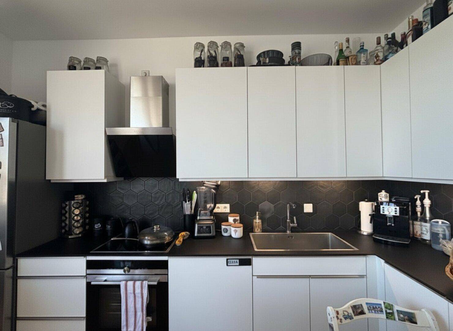 Helle Einbauküche mit weißen Fronten, schwarzer Arbeitsplatte und modernen Geräten.