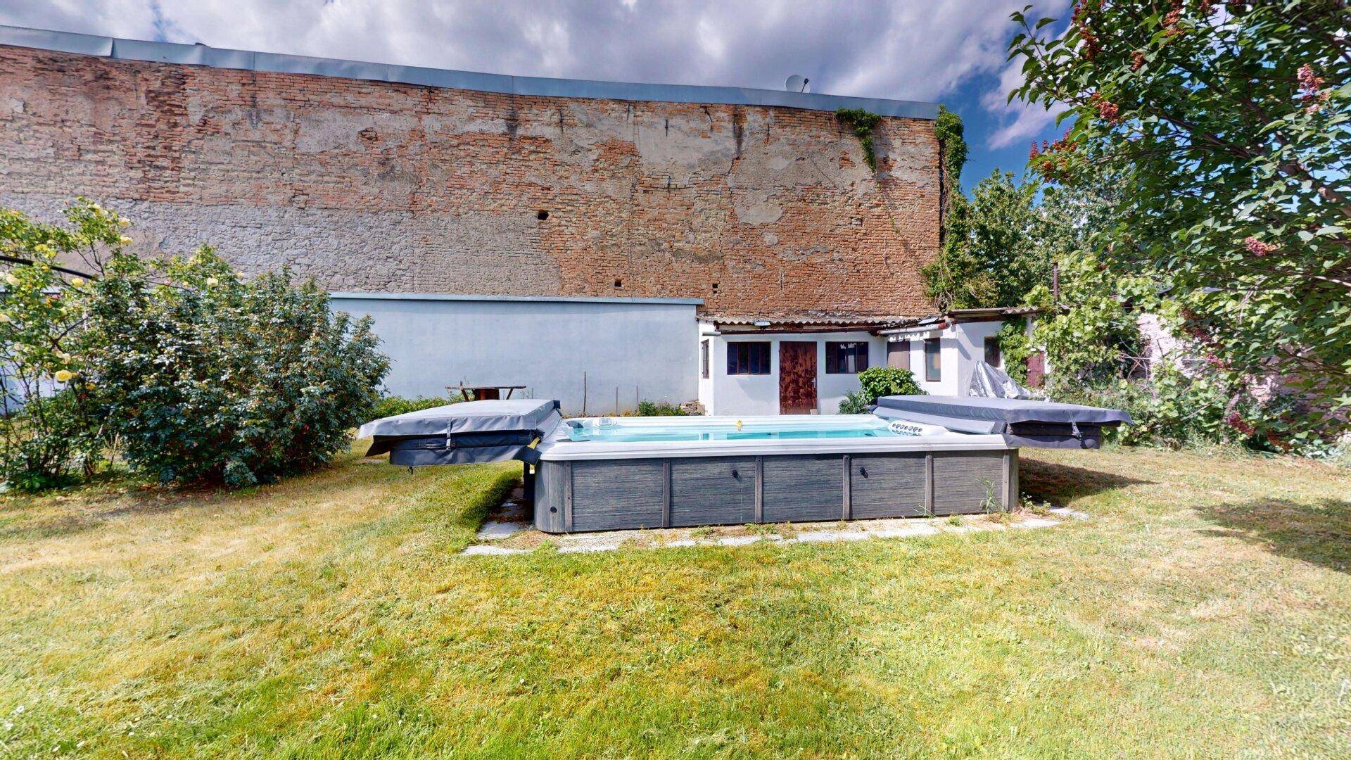 Gartenbereich mit einem eingelassenen Pool und Rasenfläche, begrenzt durch eine hohe Backsteinmauer.