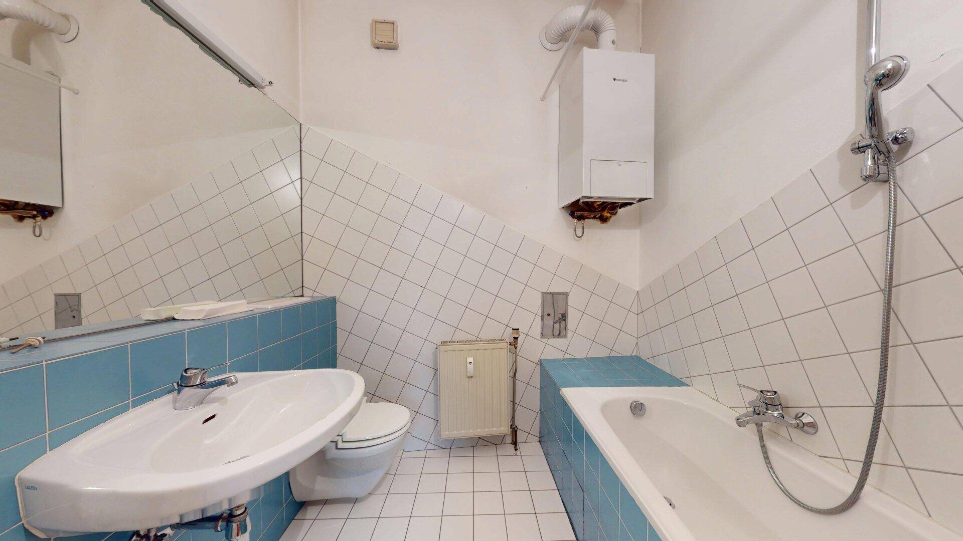 Badezimmer mit Badewanne, Waschbecken und WC, gefliest in Weiß und Hellblau, mit Gastherme.