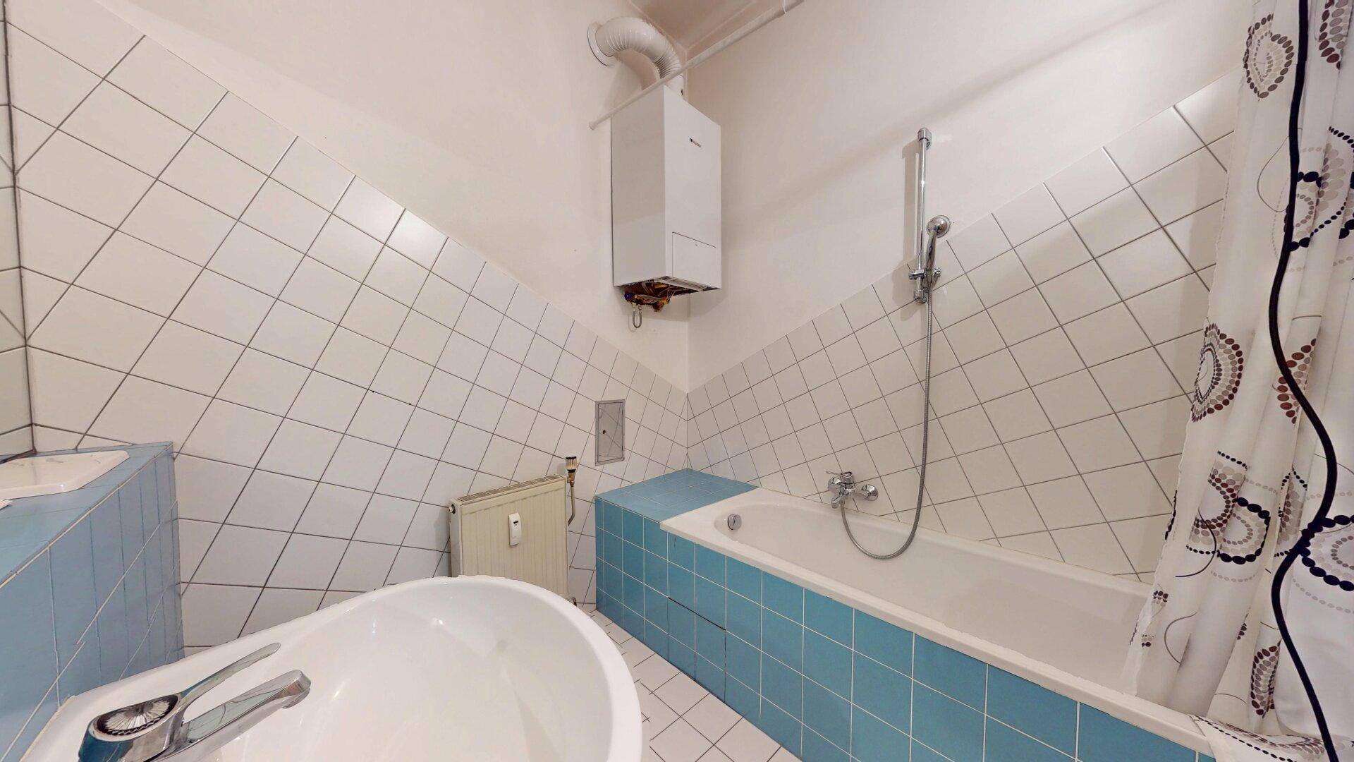 Badezimmer mit Badewanne und Duschvorrichtung, gefliest in Weiß und Hellblau, mit Gastherme.