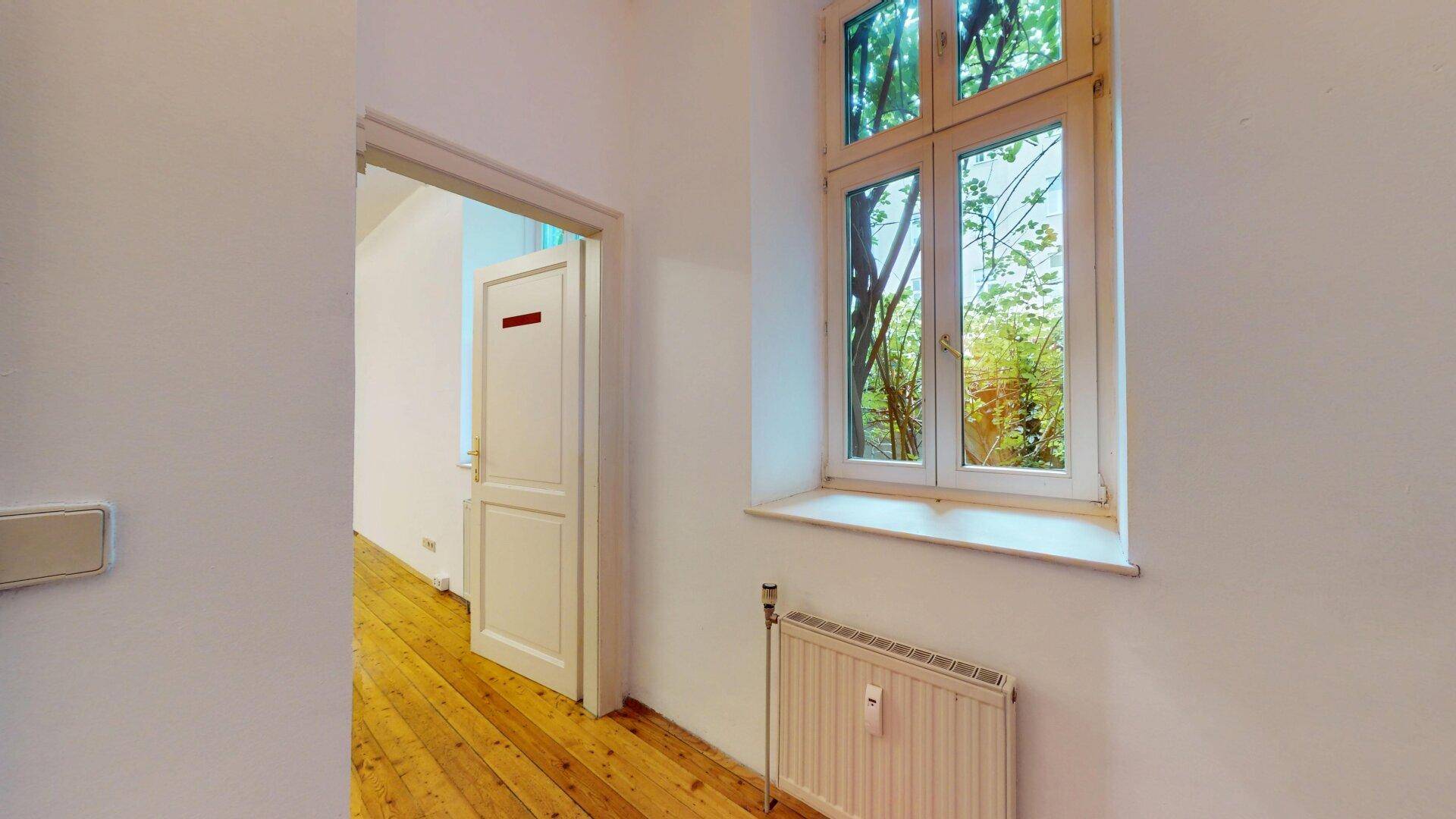 Heller Flur mit Holzfußboden und einem Fenster, das den Blick ins Grüne freigibt.