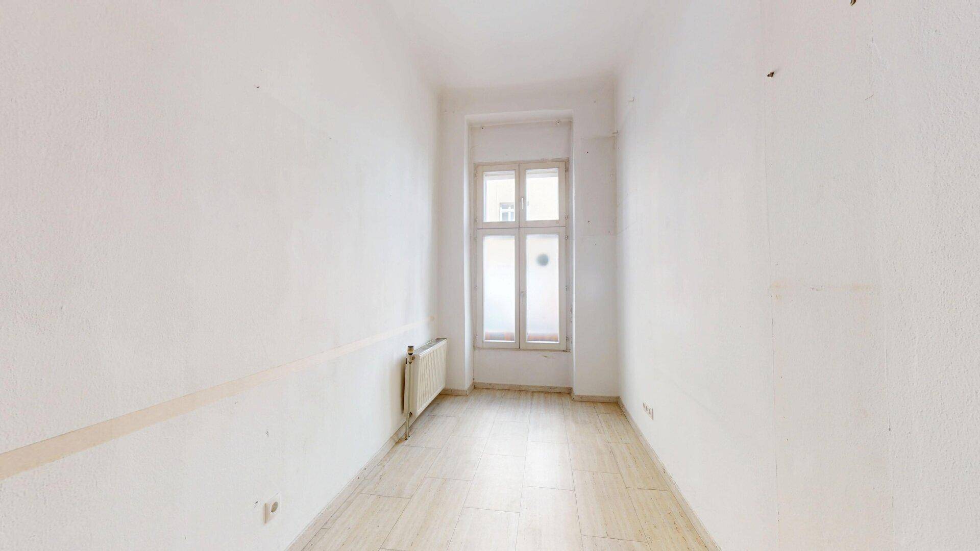 Schmaler Raum mit hellen Fliesen und einem Fenster, das den Raum mit natürlichem Licht erhellt.
