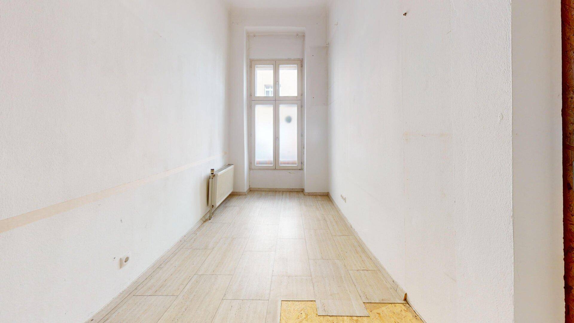 Schmaler Raum mit hellen Fliesen und einem hohen Fenster, das für ausreichend Tageslicht sorgt.
