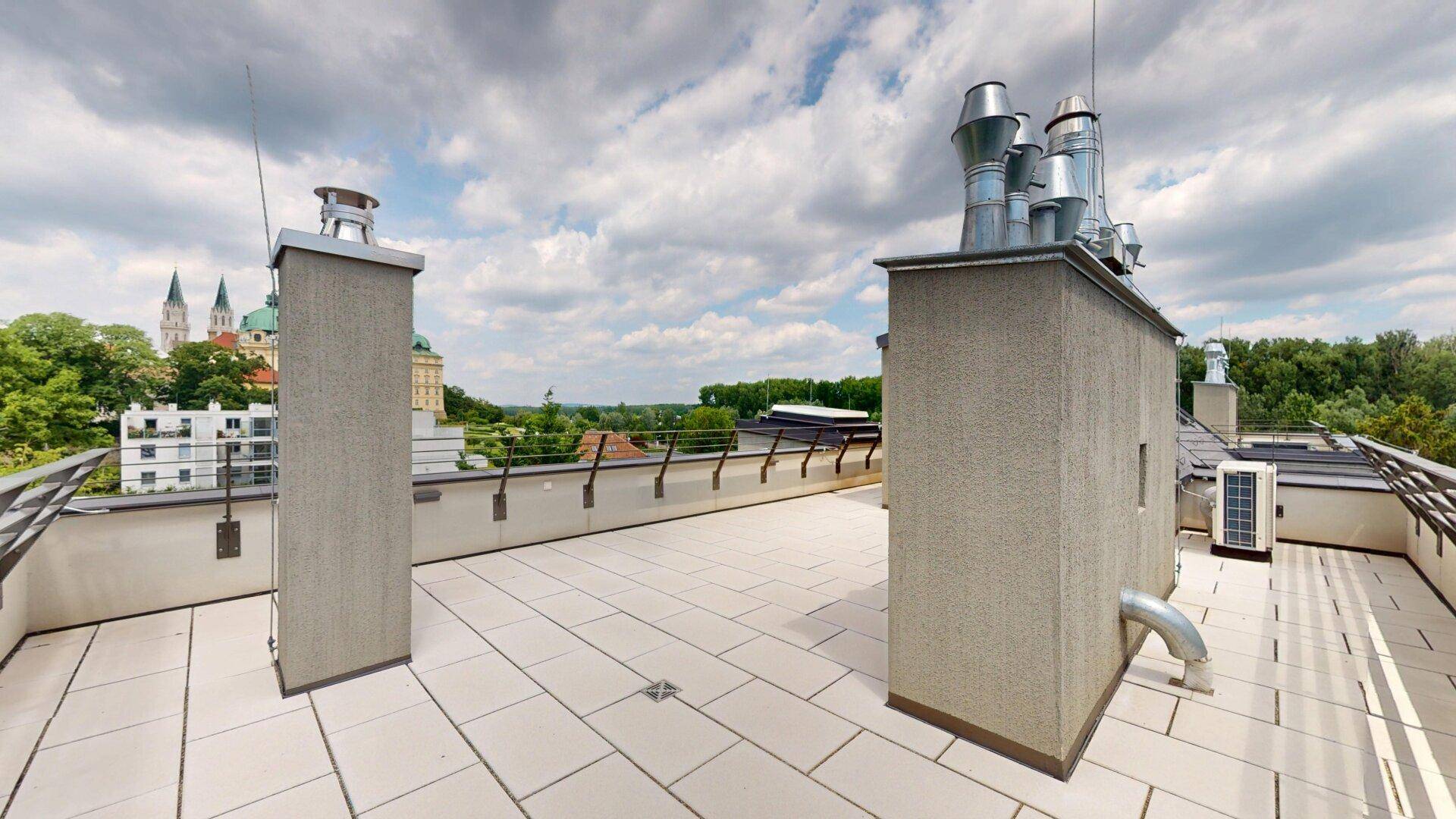 Große Dachterrasse mit Fliesenboden und weitem Blick auf die Stadt und die grüne Landschaft.