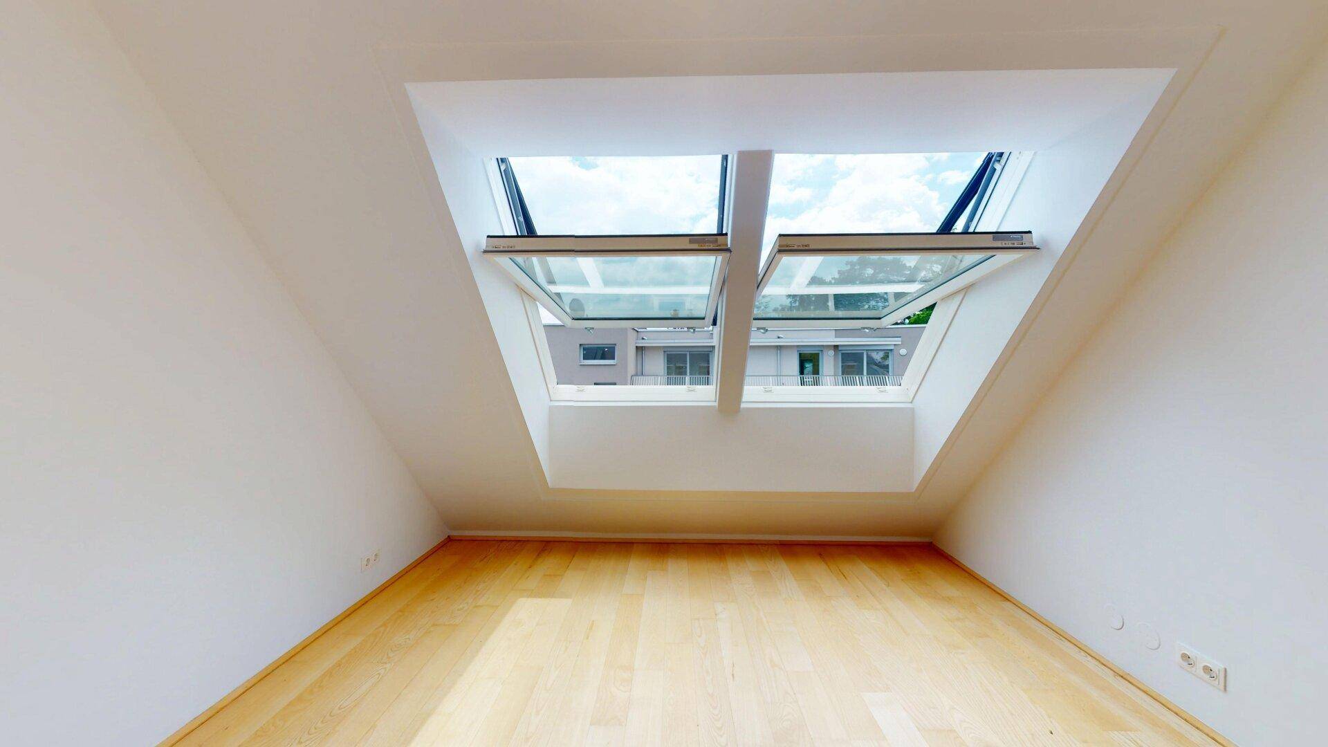Helles Zimmer im Dachgeschoss mit Holzboden und zwei großen Dachfenstern, die den Raum mit Licht füllen.
