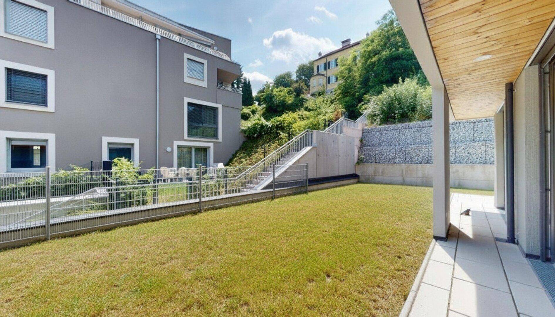 Moderne Wohnanlage mit weitläufiger Rasenfläche und Blick auf die umliegende Hügellandschaft.