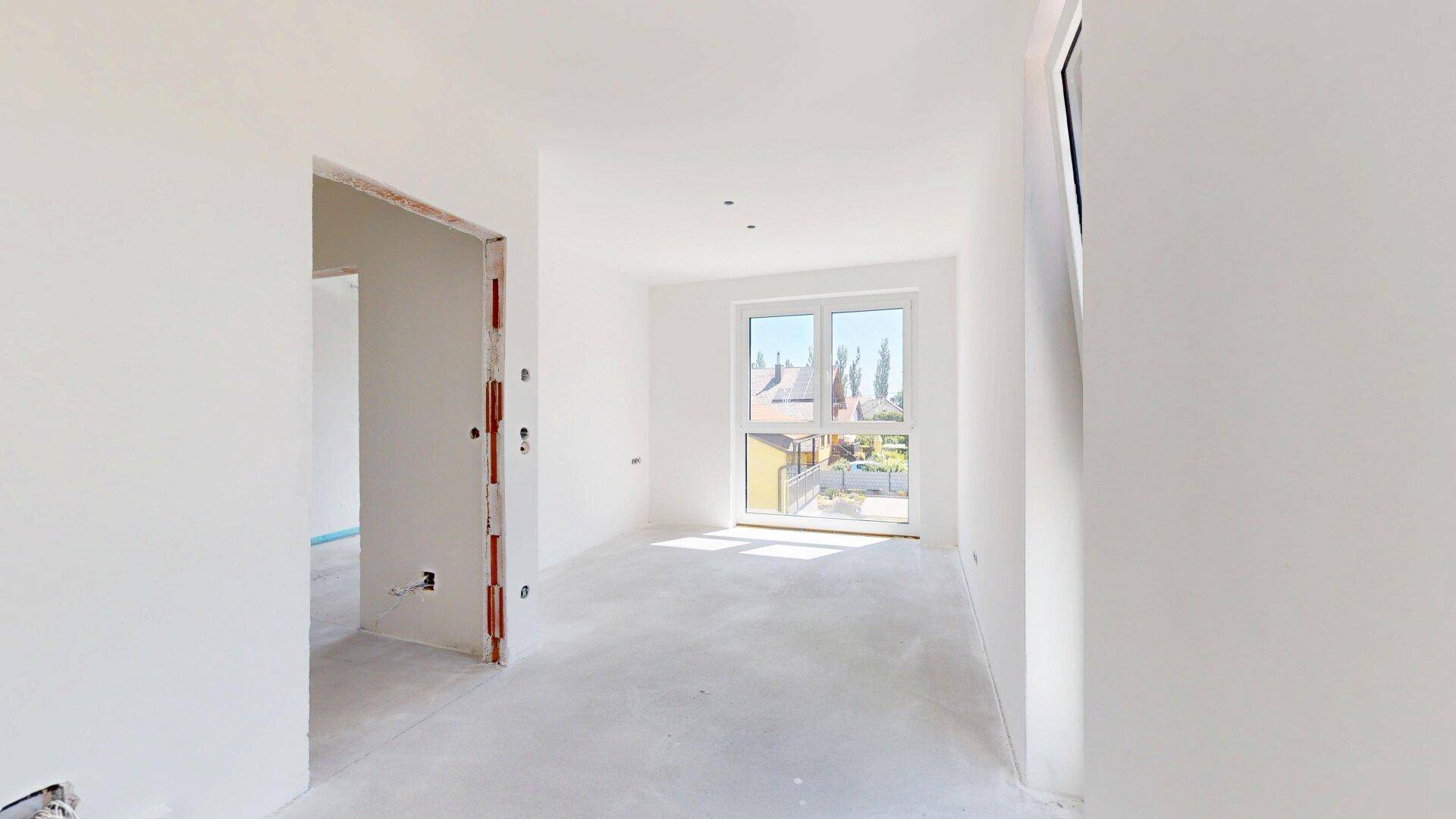 Lichtdurchflutetes, unfertiges Zimmer mit großem Fenster und Blick ins Grüne, bereit zum Ausbau.