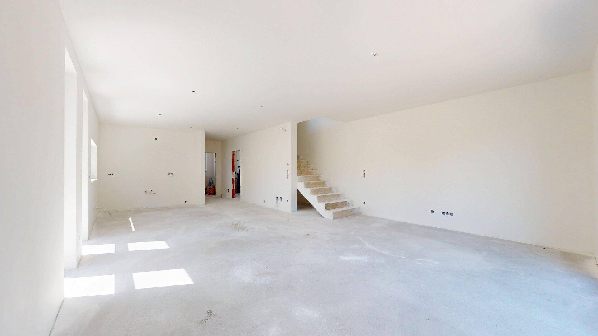 Geräumiger, unfertiger Wohnbereich mit Rohbau-Treppe und viel Tageslicht, ideal für individuelle Gestaltung.