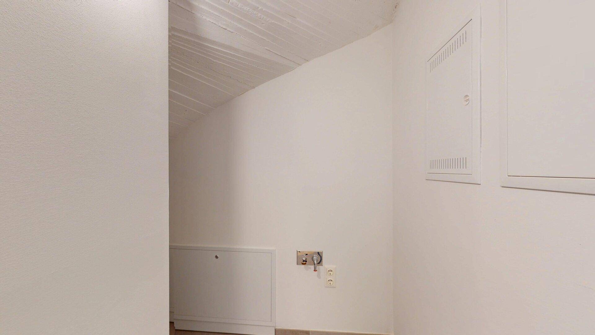 Kleiner Hauswirtschaftsraum mit schräger Decke und Zugang zu Versorgungsanschlüssen.