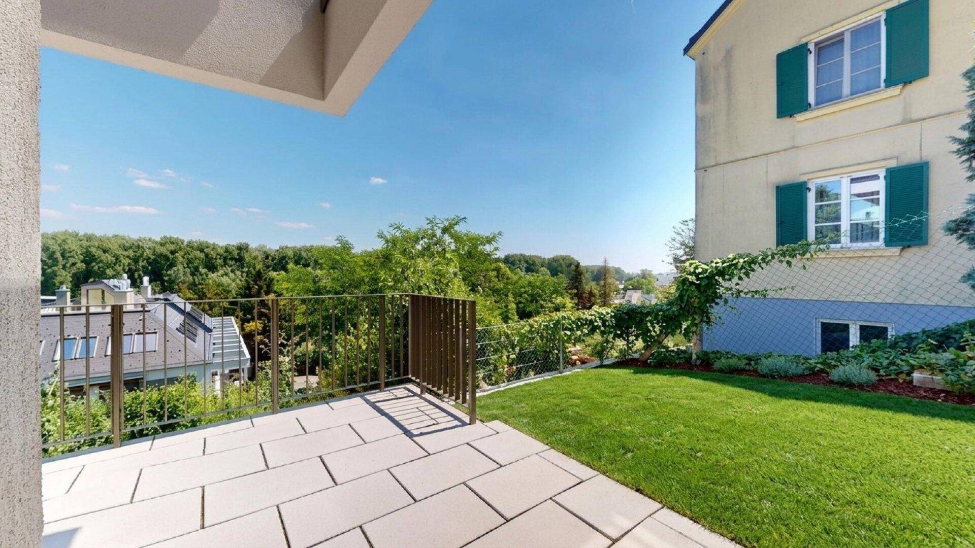 Große, gepflasterte Terrasse mit Metallgeländer und weitem Blick ins Grüne.