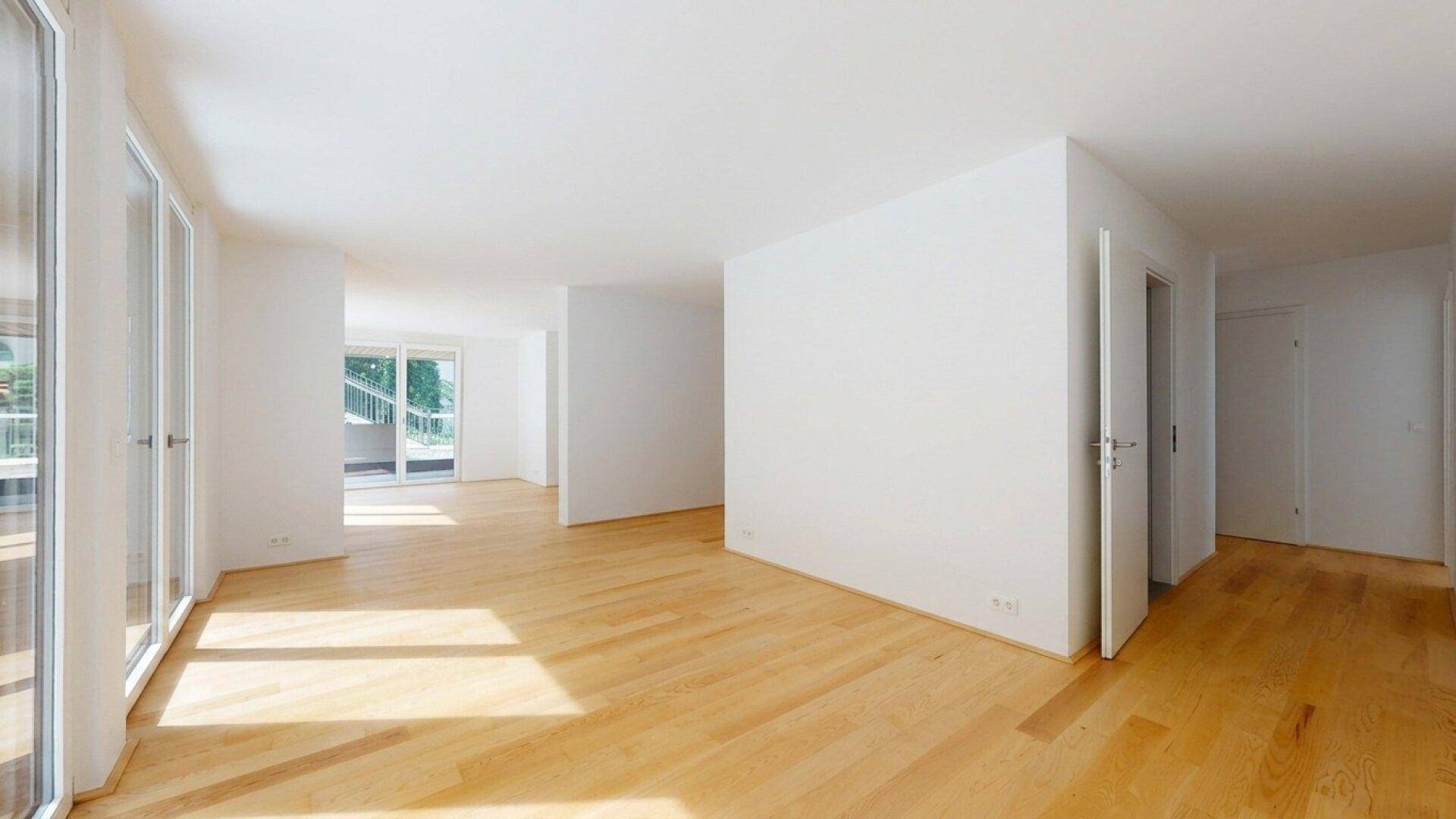 Geräumiger, heller Raum mit Holzboden und Zugang zu einem Balkon, ideal als Wohnbereich.
