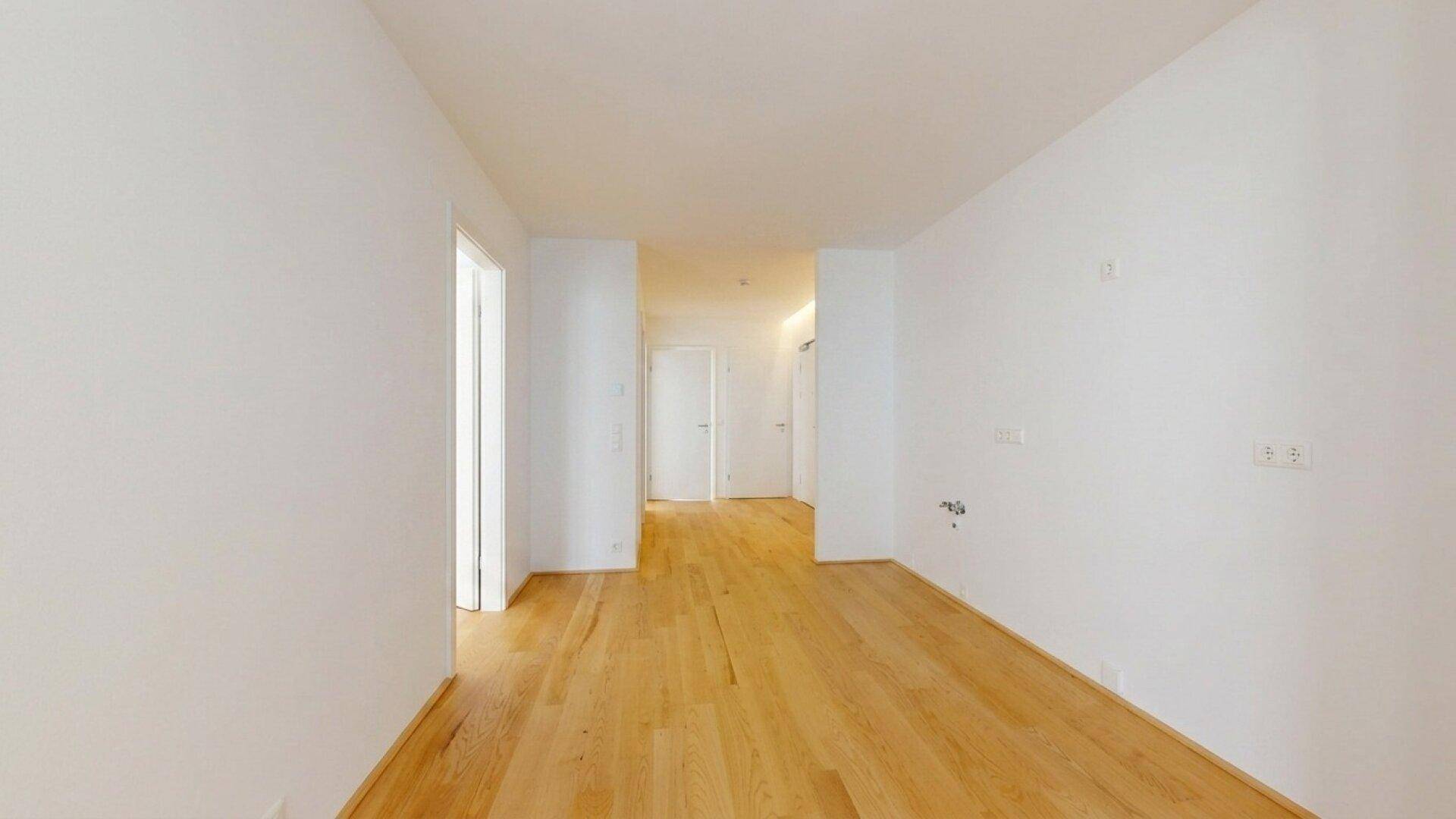 Heller Flur mit Holzboden und weißen Wänden, der zu weiteren Räumen führt.