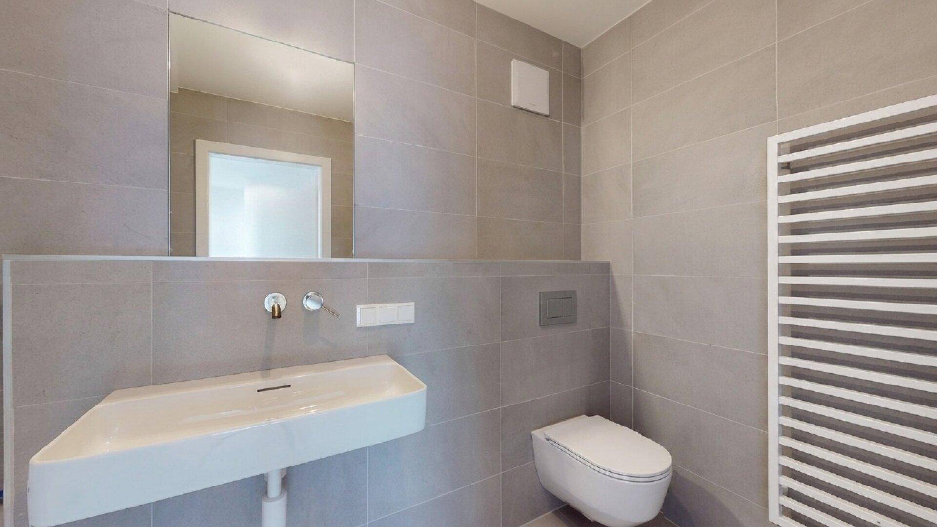 Helles Badezimmer mit modernen Fliesen, wandhängendem WC, Waschbecken und Handtuchheizkörper.