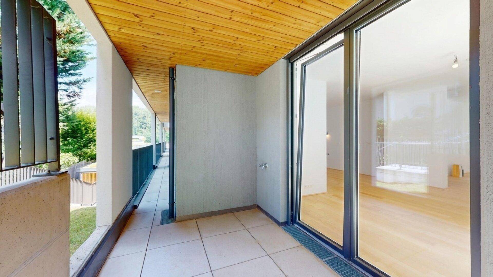 Geräumiger Balkon mit Fliesenboden und Holzdach, direktem Zugang zum Innenbereich.