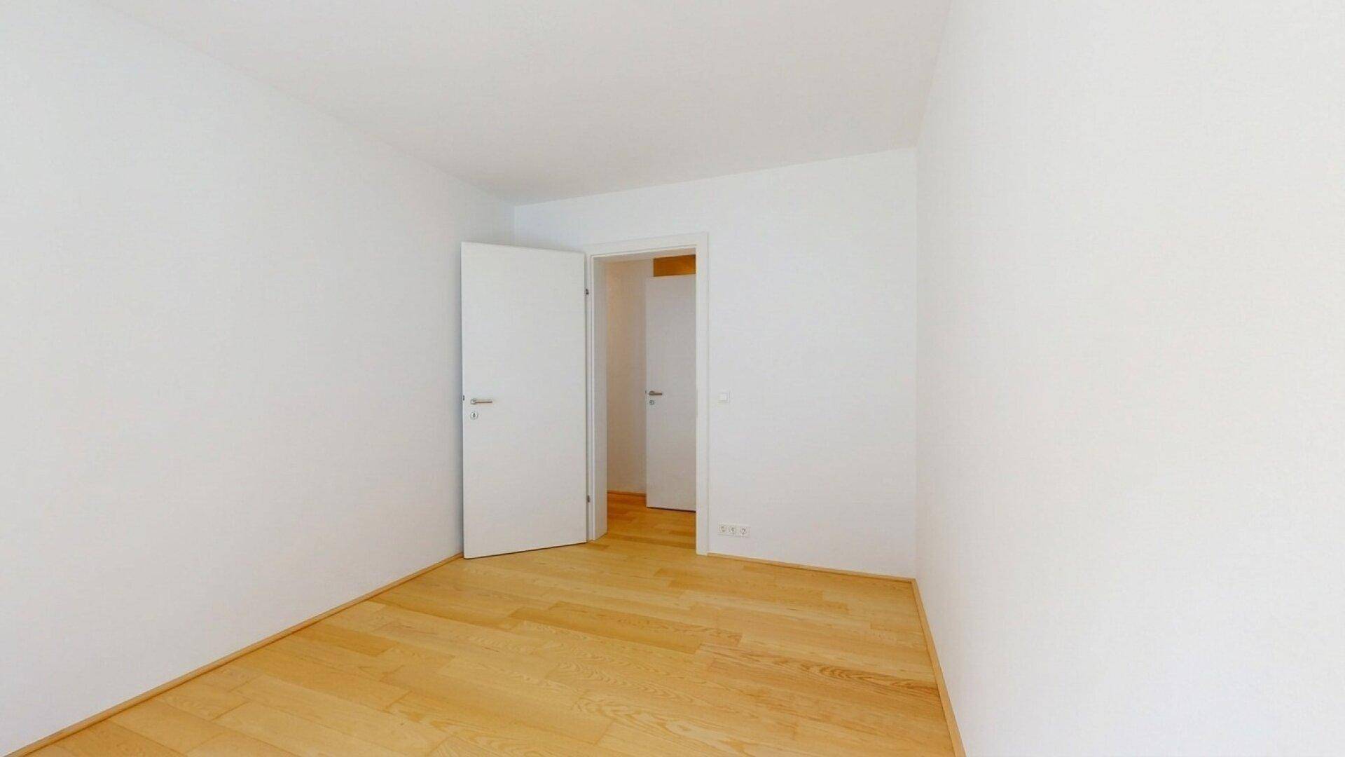 Schlichtes Zimmer mit Holzboden und weißen Wänden, bereit für individuelle Einrichtung.