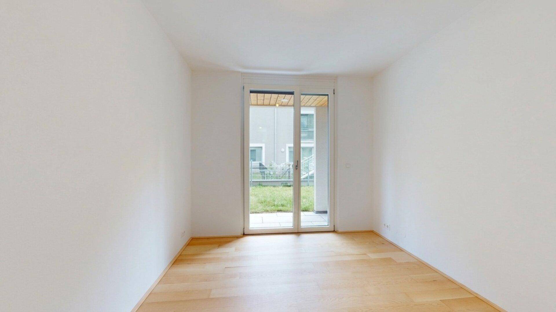 Helles Zimmer mit Holzboden und Zugang zu einem kleinen Außenbereich mit Rasen.