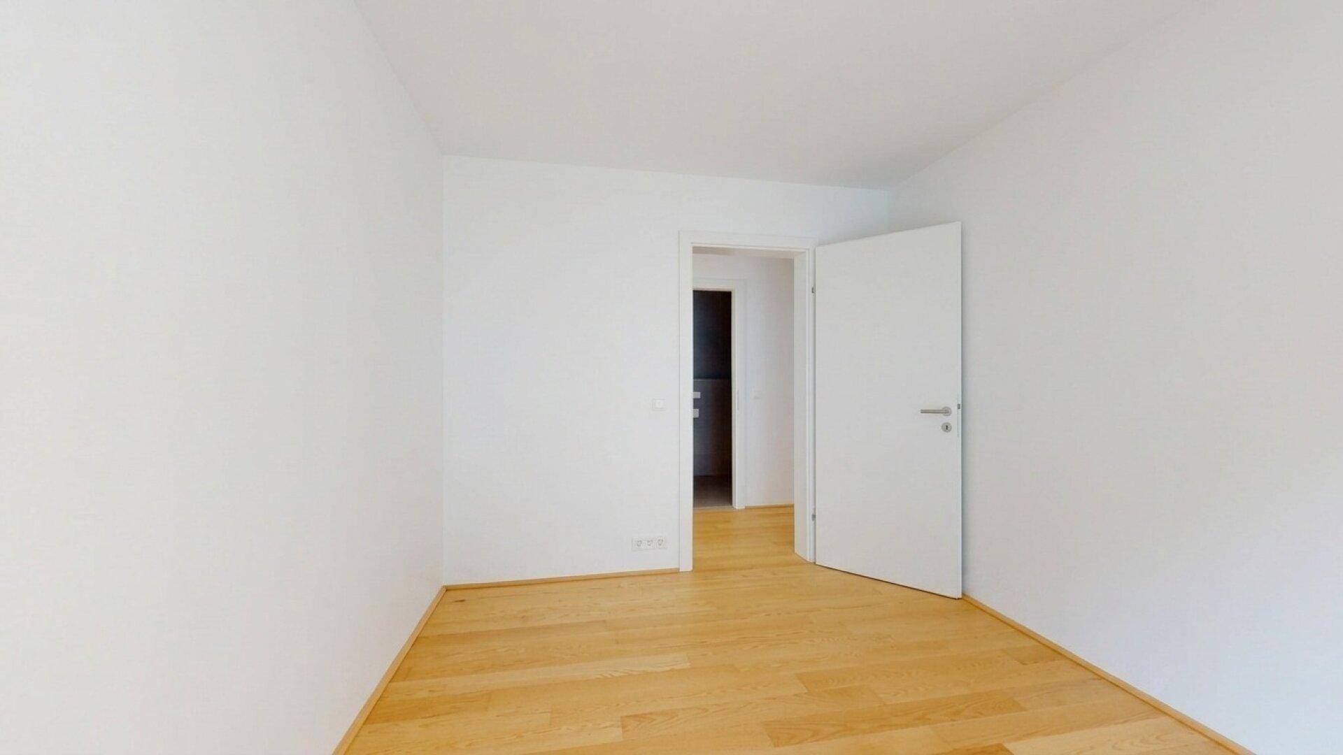 Schlichtes Zimmer mit Holzboden und weißen Wänden, ideal als Schlaf- oder Arbeitszimmer.