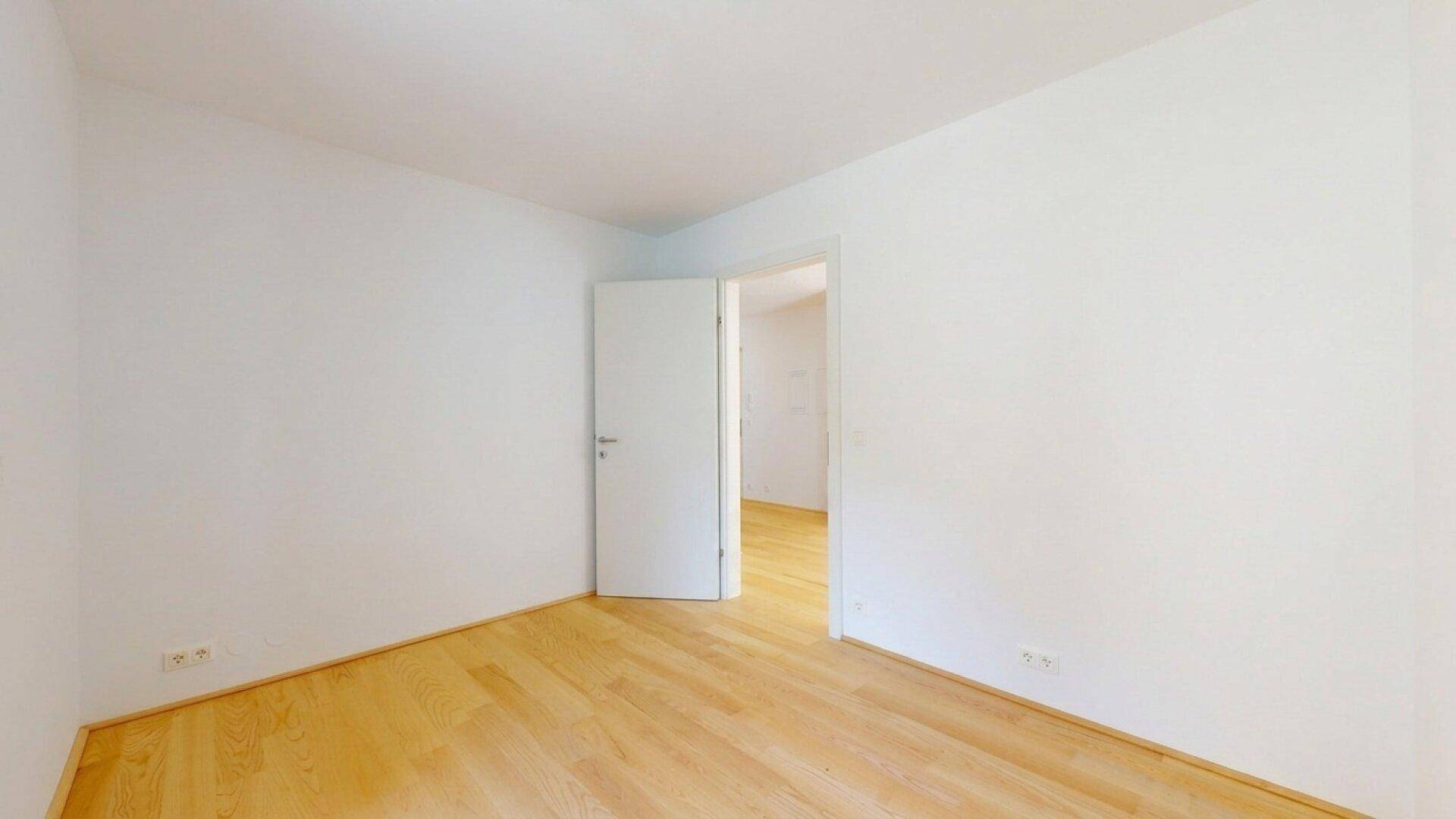 Leeres Zimmer mit Holzboden und weißen Wänden, das vielseitig genutzt werden kann.