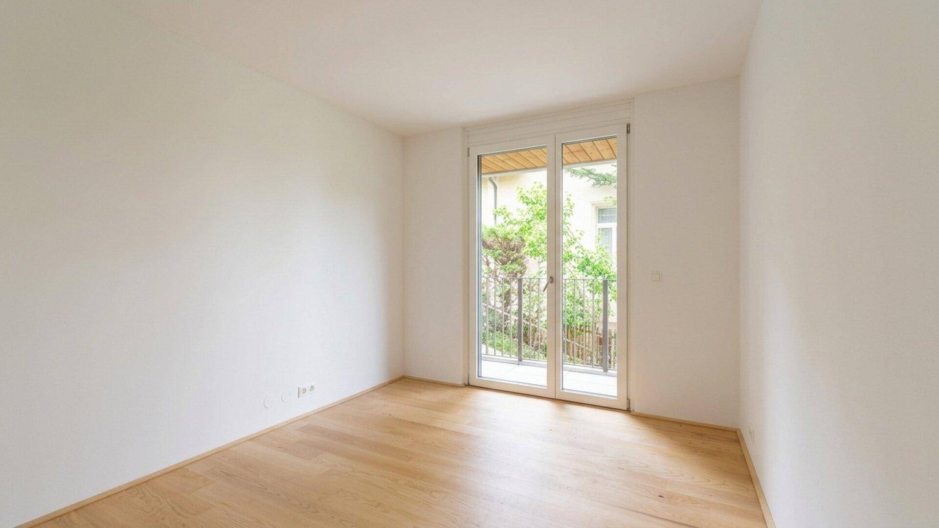 Freundliches Zimmer mit Parkettboden und Fensterfront, die viel Tageslicht hereinlässt.