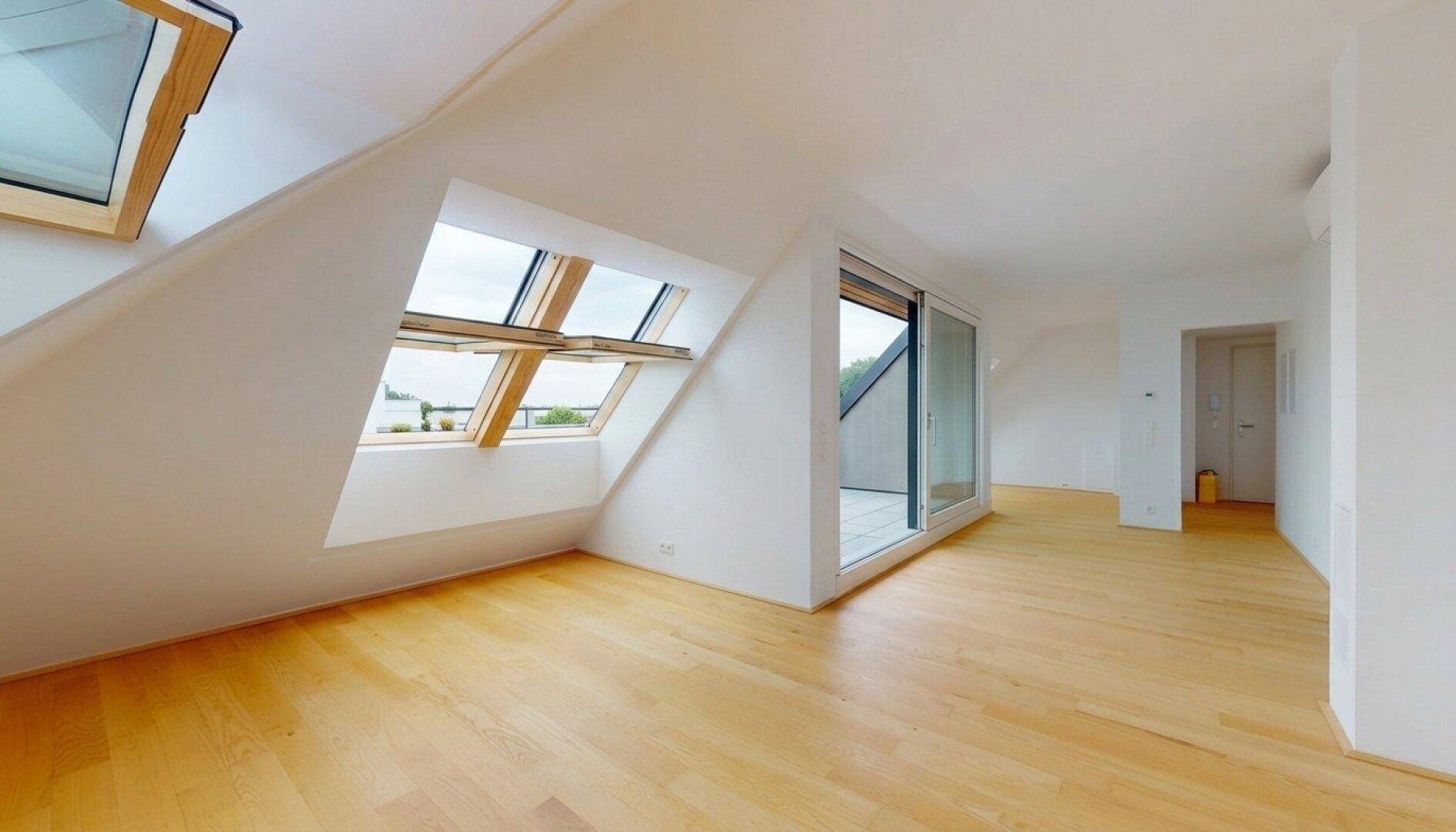 Heller Wohnraum im Dachgeschoss mit Holzboden, Dachfenstern und Zugang zur Außenterrasse.