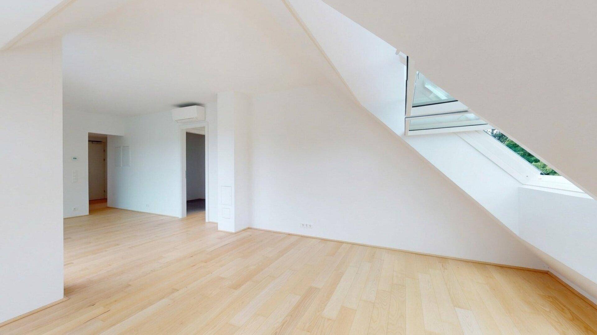 Geräumiger, heller Raum mit Holzboden und schrägen Wänden, ausgestattet mit Klimaanlage.