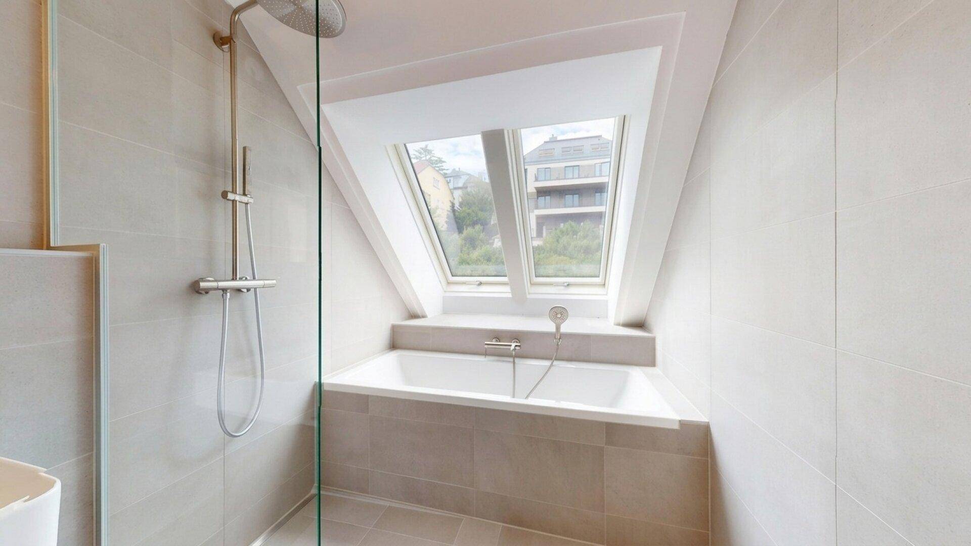 Badezimmer mit Badewanne unter einem Dachfenster und einer modernen Duschkabine.