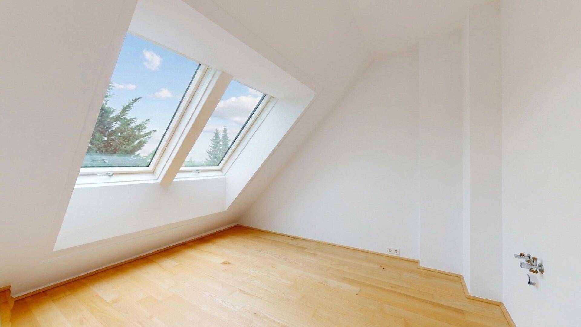 Helles Zimmer im Dachgeschoss mit Holzboden und zwei großen Dachfenstern, die viel Sonnenlicht bieten.