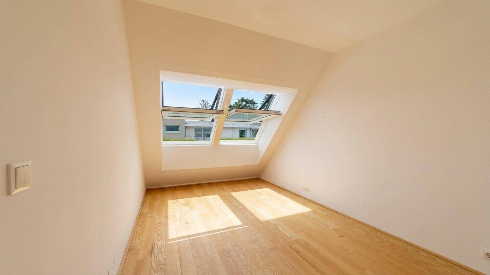 Geräumiges Zimmer mit Holzboden und Dachfenstern, die den Raum mit natürlichem Licht durchfluten.