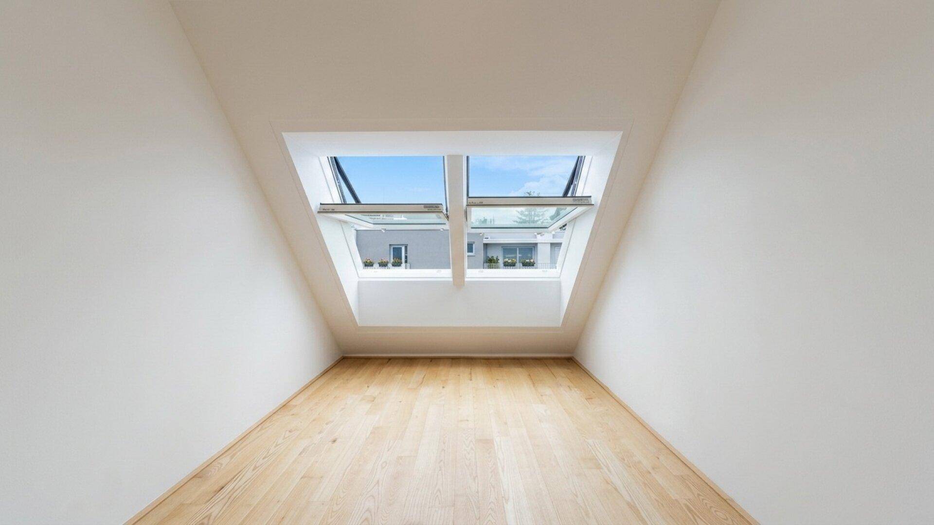 Heller Raum im Dachgeschoss mit Holzboden und zwei großen Dachfenstern, die den Raum erhellen.