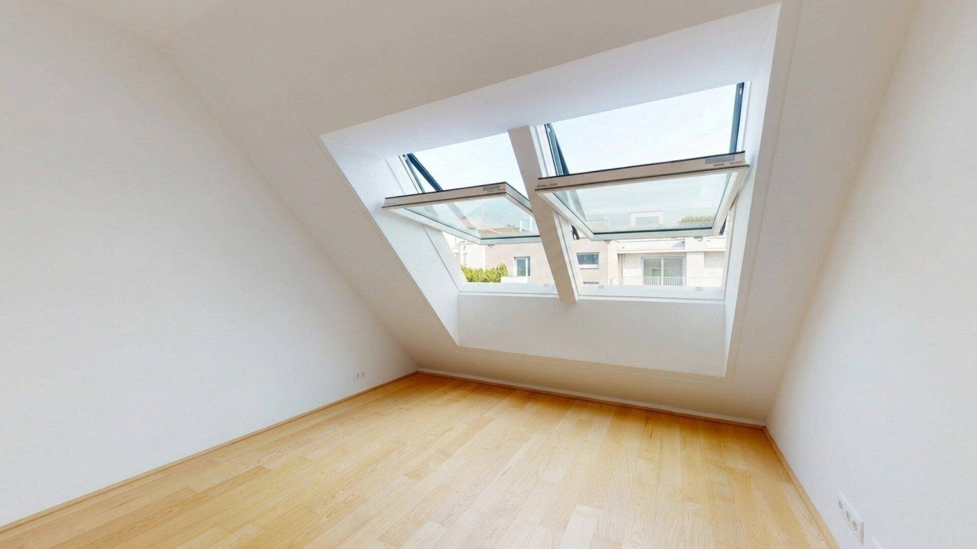 Zimmer im Dachgeschoss mit Holzboden und Dachfenstern, die einen Blick nach draußen ermöglichen.