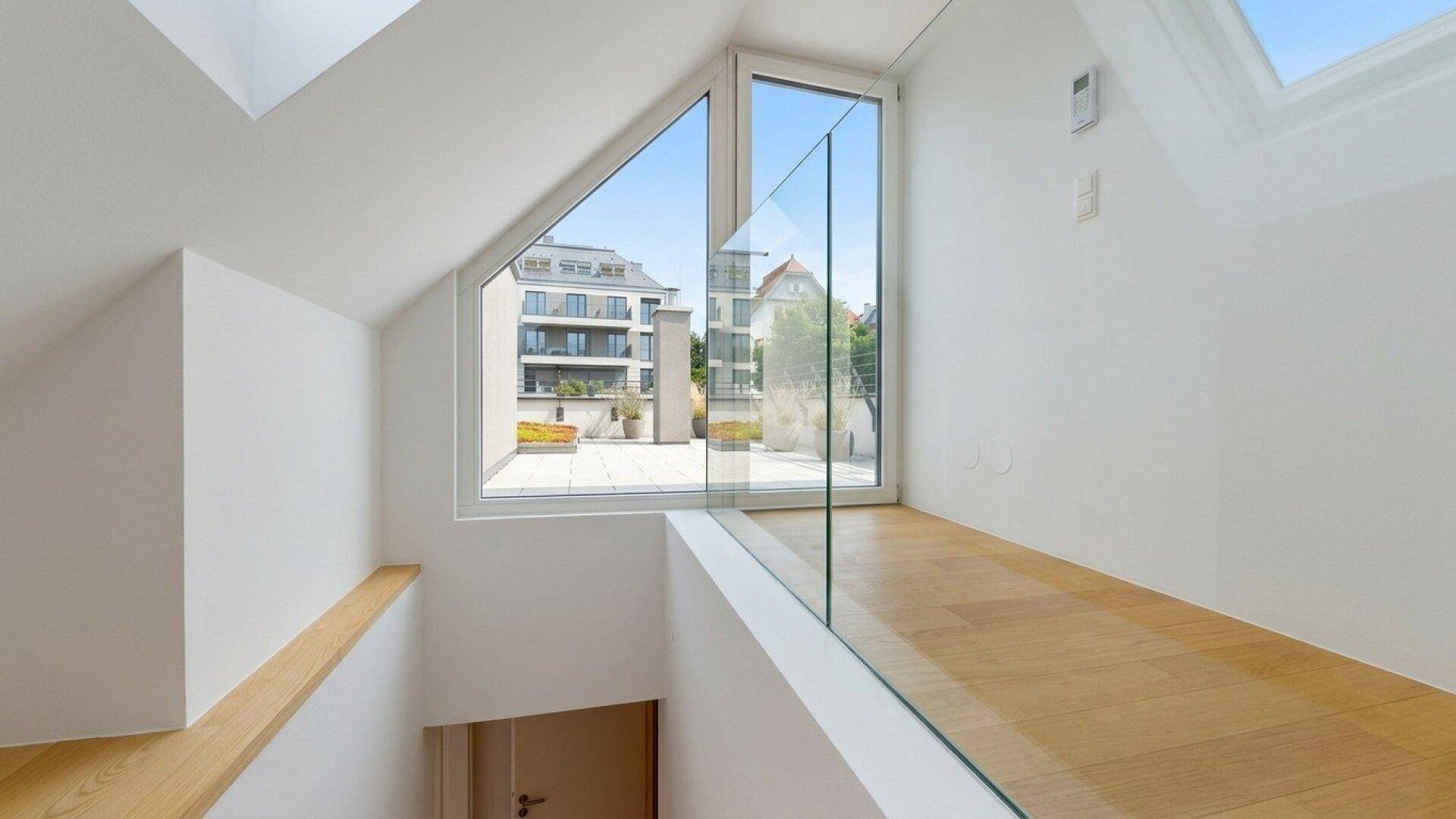 Heller Treppenabsatz mit Glasgeländer und großen Fenstern, die einen weiten Blick bieten.