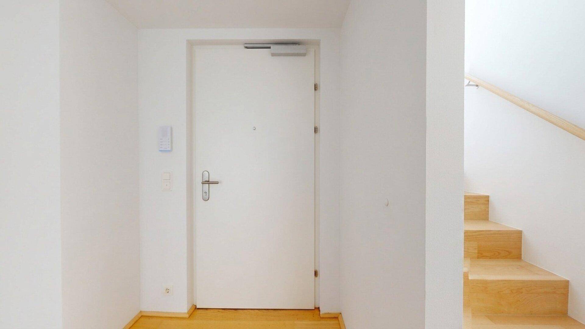 Eingangsbereich mit heller Holztür und Treppe, die zu den oberen Etagen führt.