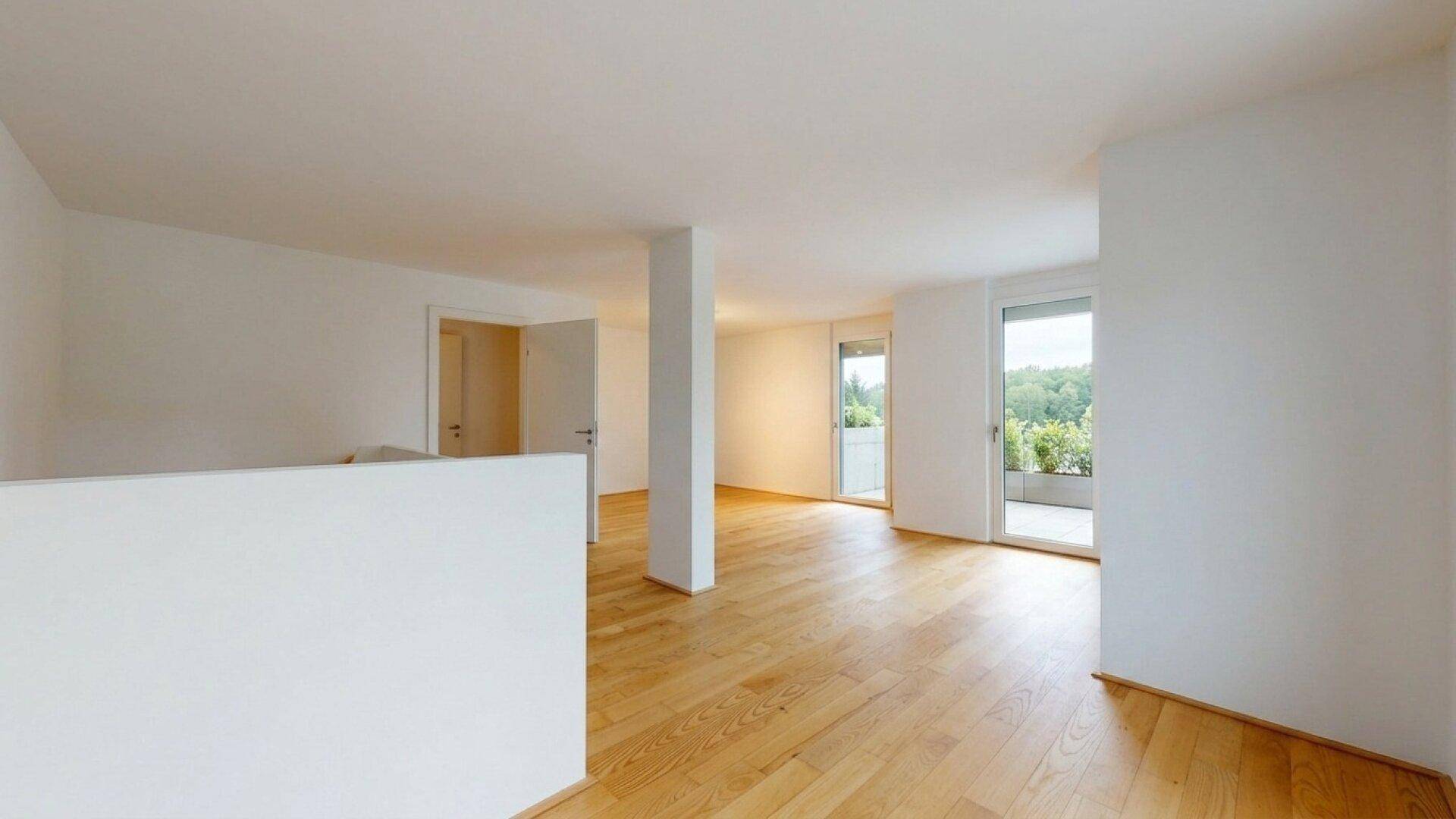 Geräumiger, heller Wohnbereich mit Holzboden und Zugang zu einem Balkon.