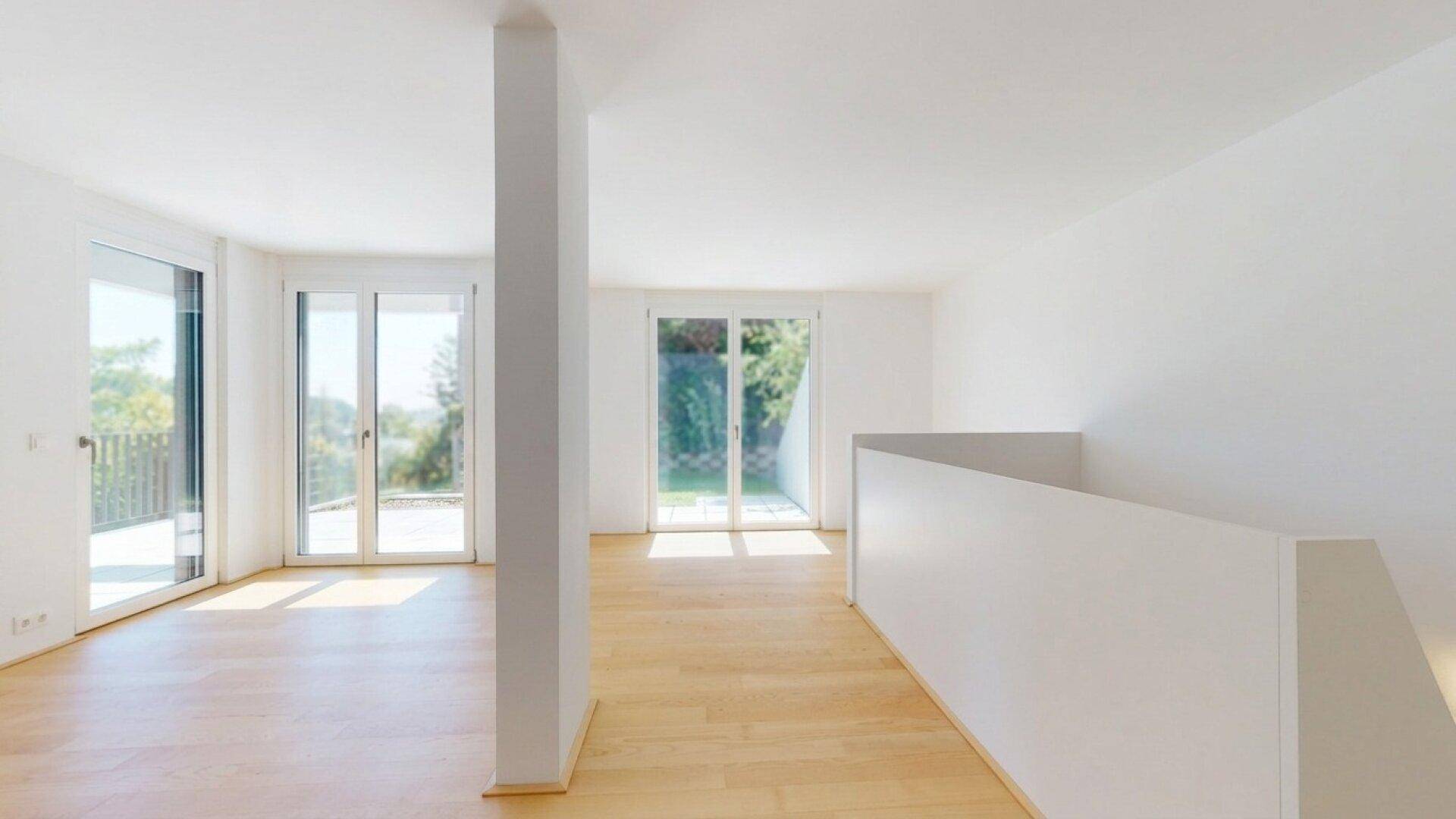 Lichtdurchfluteter, offener Wohnbereich mit Holzboden und mehreren Fenstern.