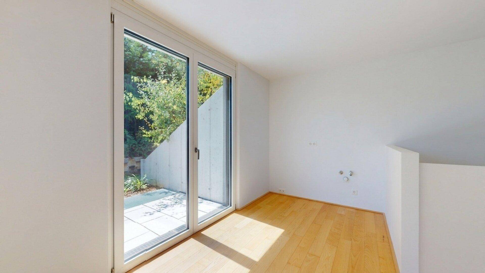 Helles Zimmer mit Holzboden und Zugang zu einer kleinen Außenterrasse.