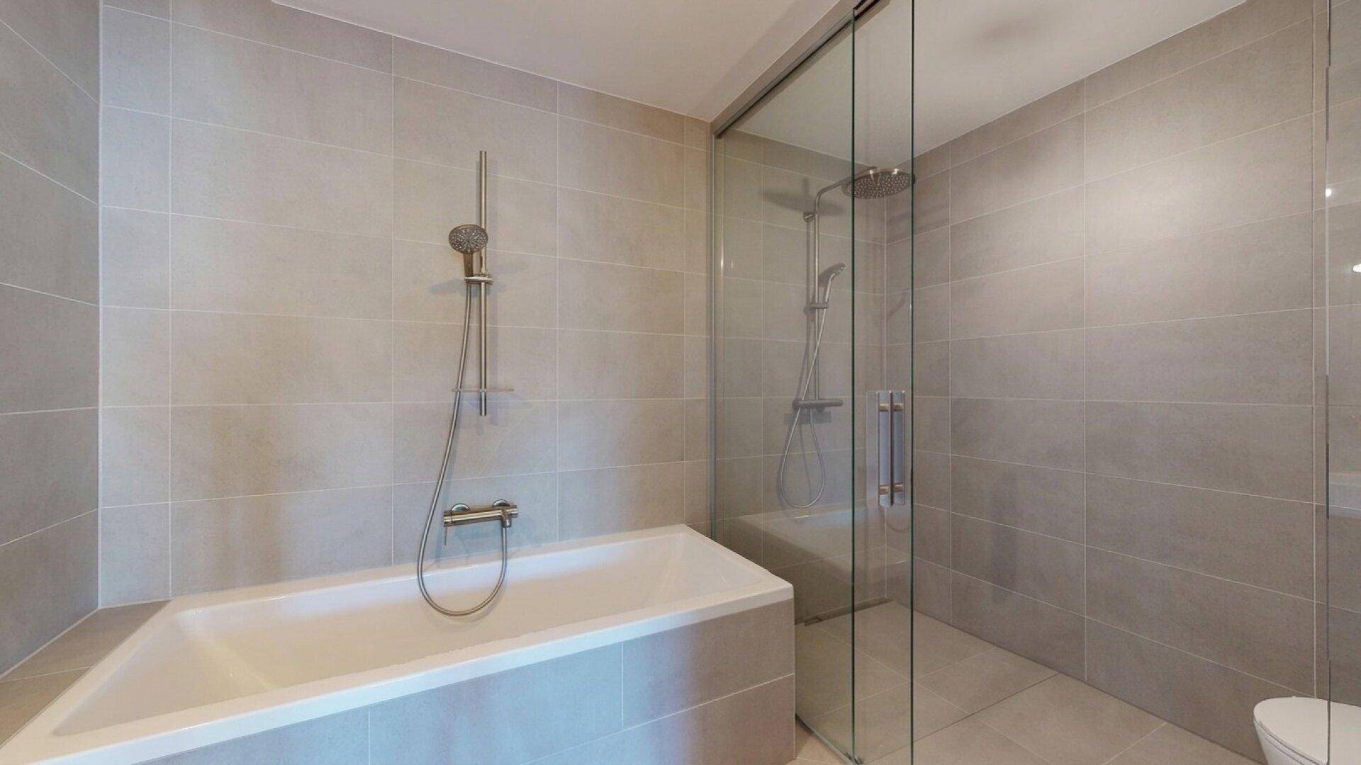 Modernes Badezimmer mit Badewanne, Glasdusche und hellgrauen Fliesen.