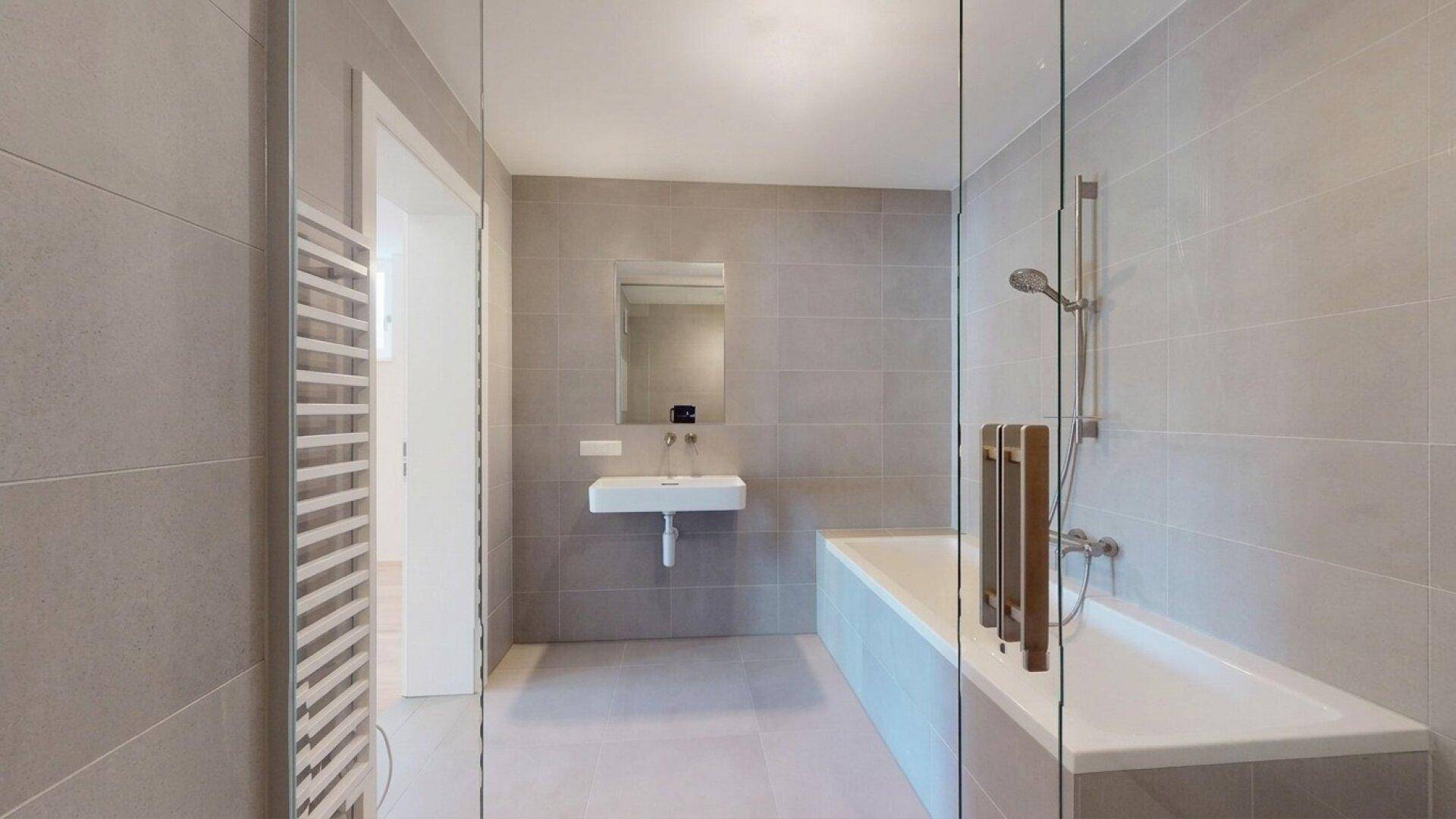 Helles Badezimmer mit Badewanne, Dusche, Einzelwaschbecken und beheiztem Handtuchhalter.