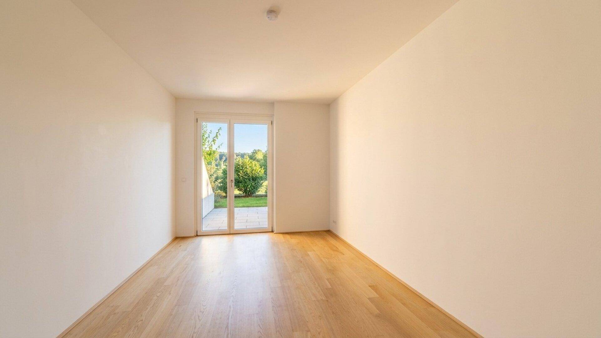 Helles Zimmer mit Holzboden und Zugang zu einem privaten Gartenbereich.