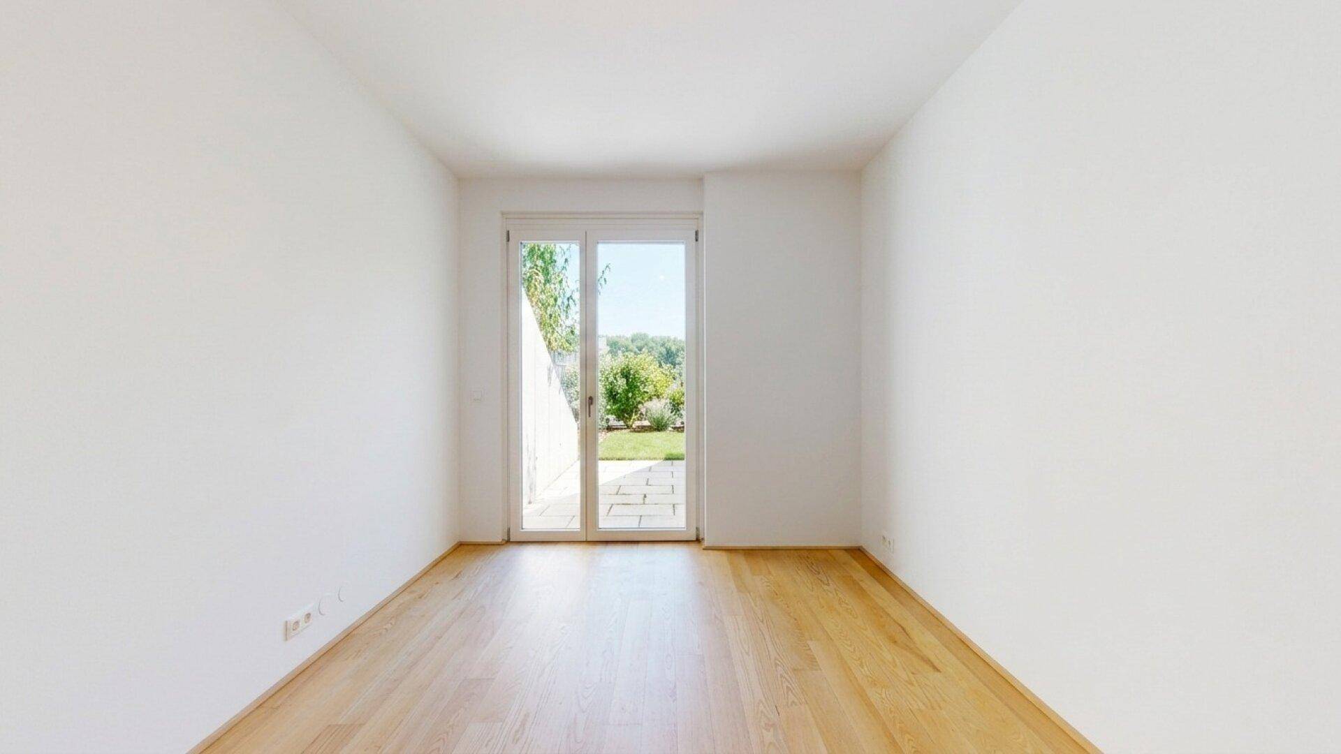 Geräumiges Zimmer mit Holzboden und großen Fenstern zum Garten.