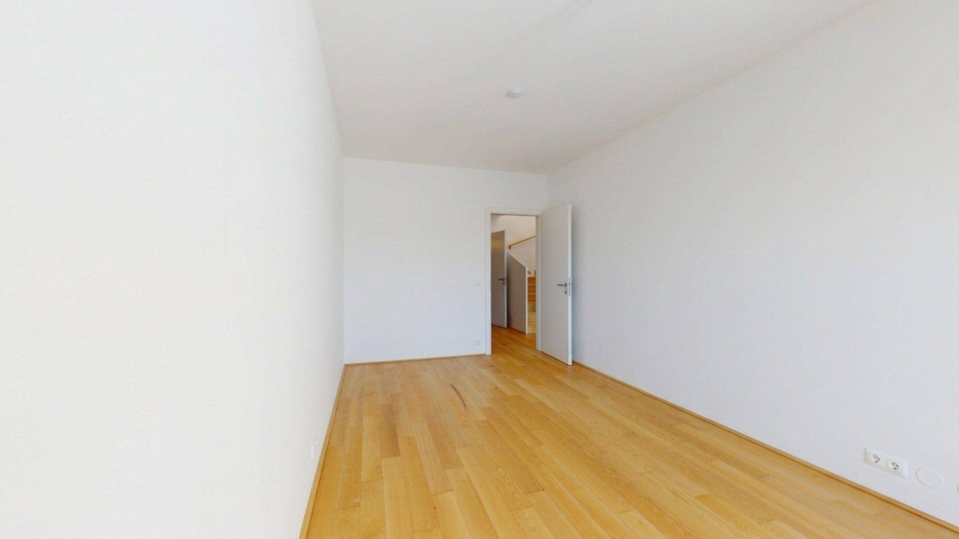 Leeres Zimmer mit Holzboden und weiß gestrichenen Wänden, ideal als Schlafzimmer.