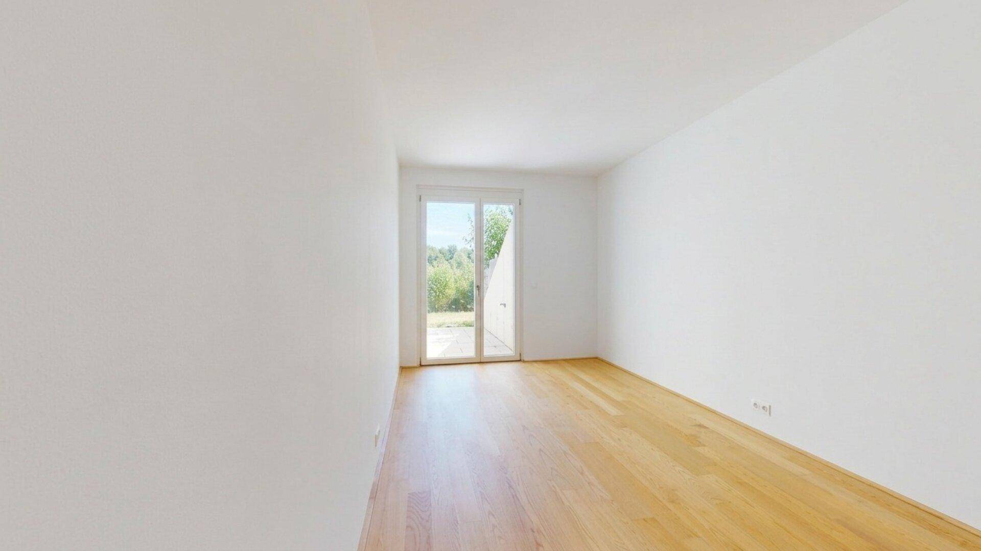 Helles Zimmer mit Holzboden und Zugang zu einem kleinen Gartenbereich.