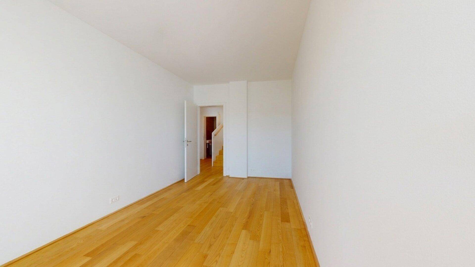 Leeres Zimmer mit Holzboden und weiß gestrichenen Wänden, bereit zur Einrichtung.