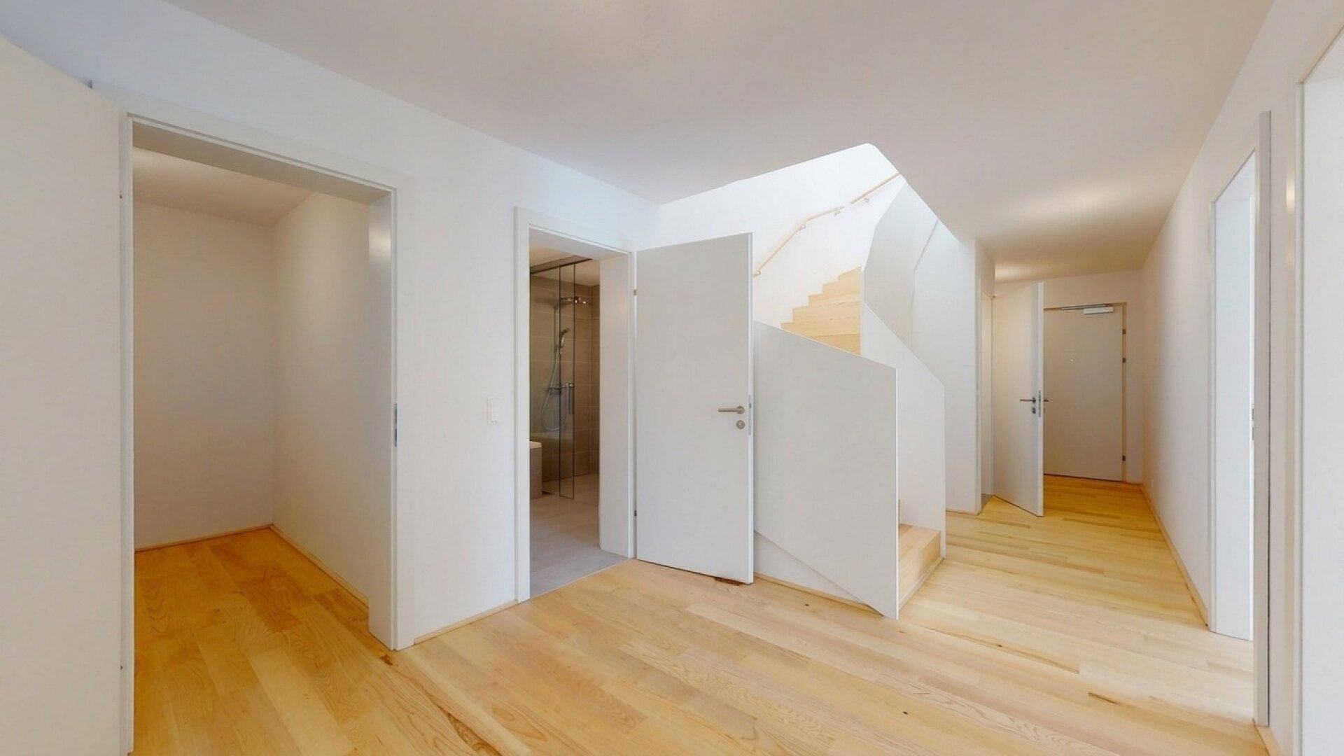 Heller Flur mit Holztreppe und Zugang zu verschiedenen Räumen.