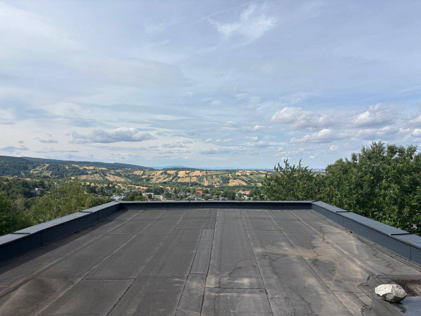 Flachdach mit Panoramablick über die grüne, hügelige Landschaft unter bewölktem Himmel.