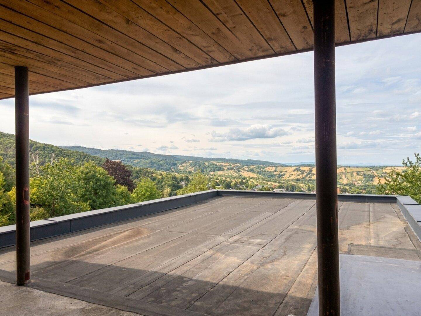 Überdachte Terrasse mit Holzdach und weitem Blick über die hügelige Landschaft.