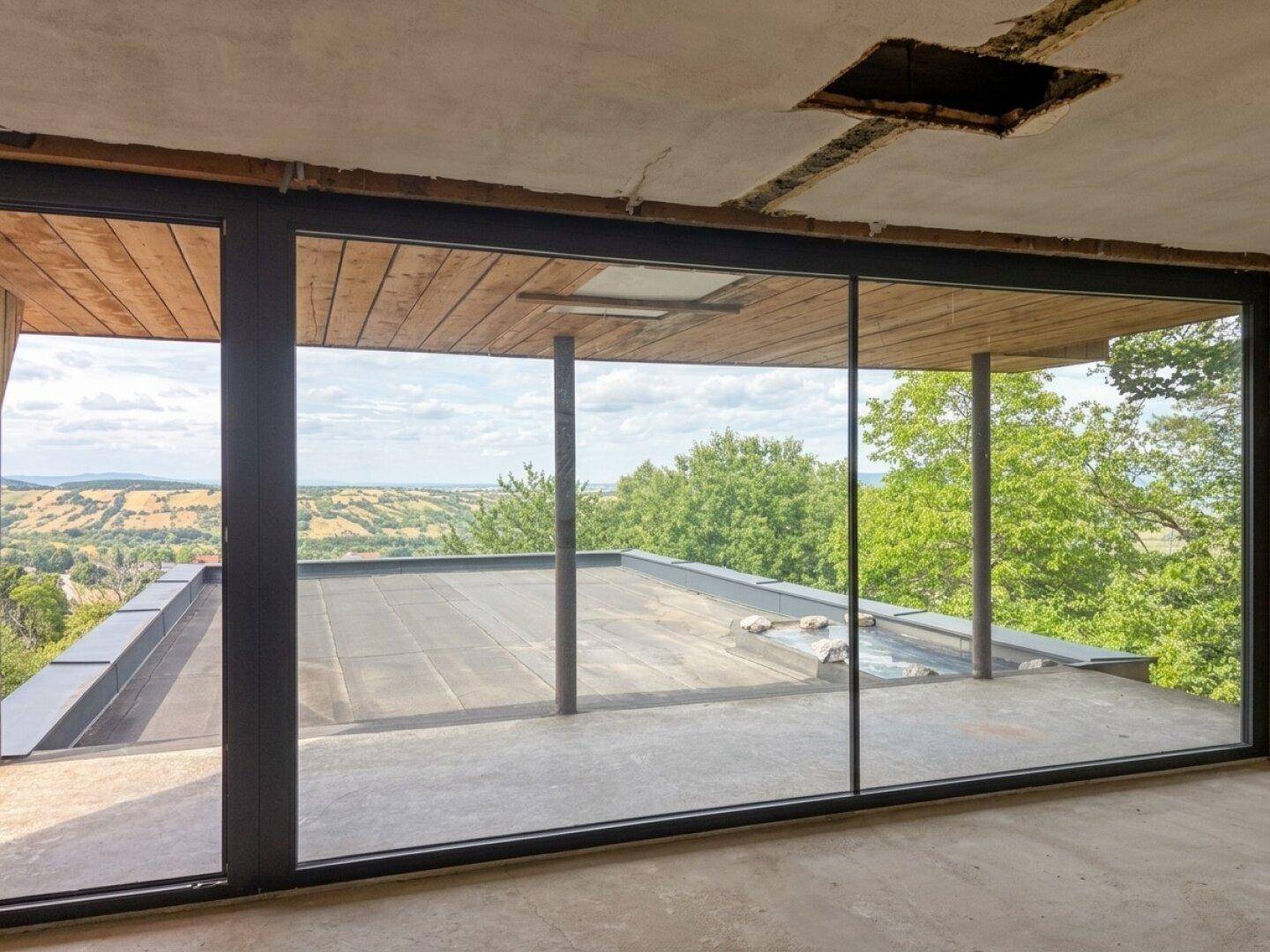 Innenraum im Rohbau mit großen Glasschiebetüren und weitem Blick auf die Landschaft.