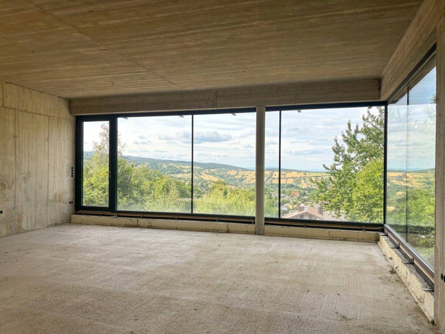 Rohbau-Innenraum mit großen Panoramafenstern und beeindruckendem Blick auf die Natur.