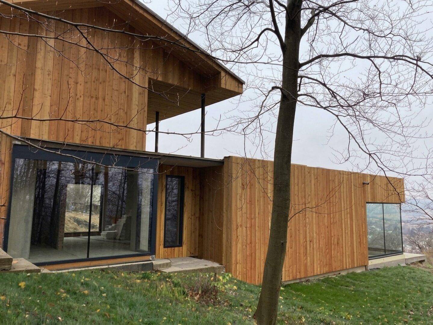 Modernes Haus mit Holzfassade und großen Glasflächen, eingebettet in eine natürliche Hanglage.