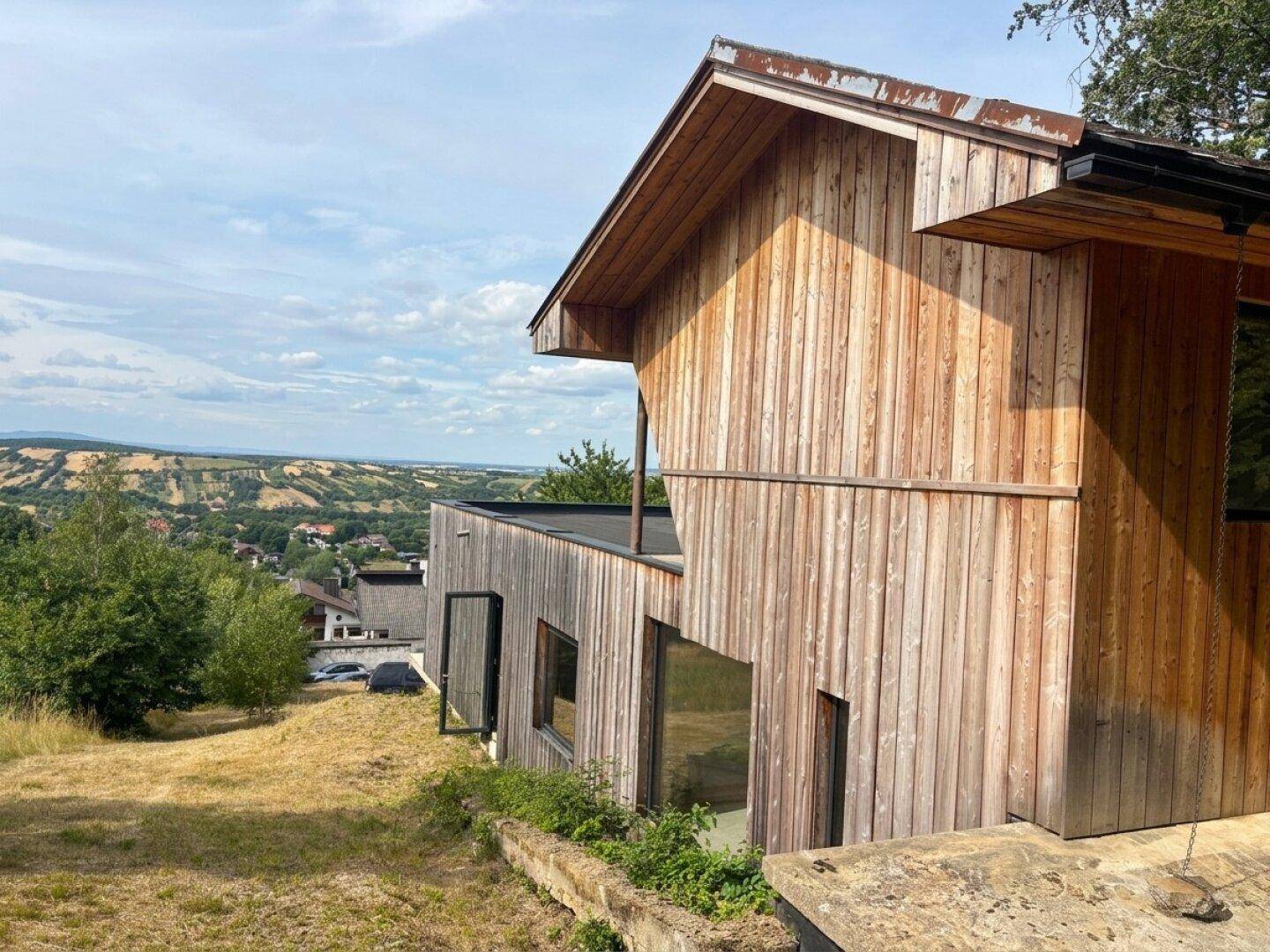 Seitenansicht des modernen Holzhauses mit Flachdach und weitem Blick über die Landschaft.
